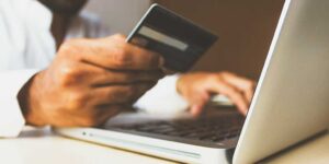 close de uma mão masculina segurando um cartão de crédito e realizando uma compra no notebook